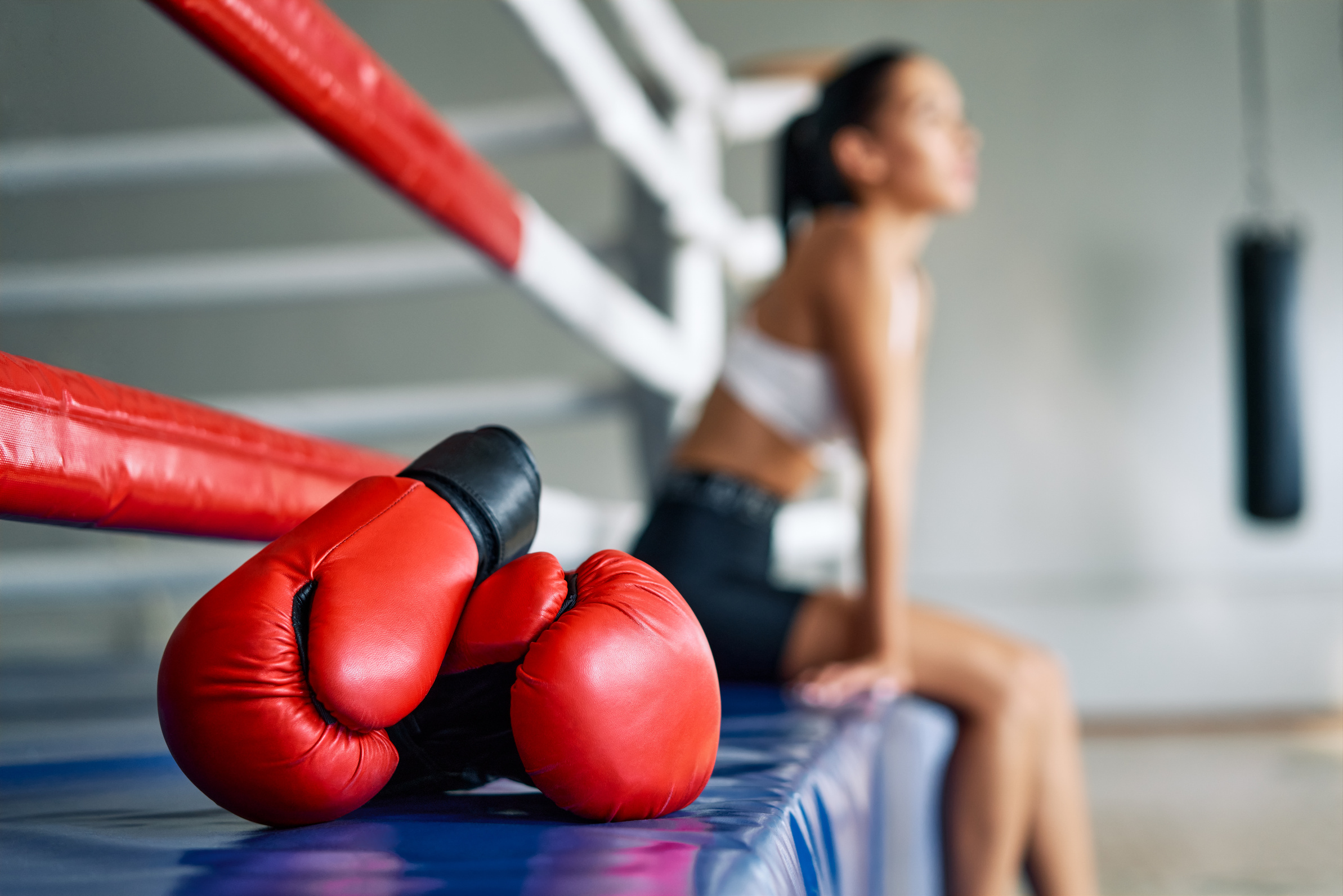 Rote Boxhandschuhe auf einer Trainingsmatte, im Hintergrund eine sitzende Person